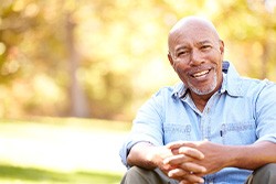 Senior man in denim jacket sitting outside with hands folded