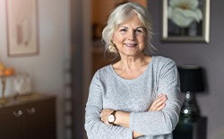 Senior woman in grey shirt smiling with arms folded