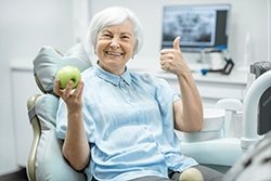 Woman with apple gives thumbs up for dental implants in Texarkana