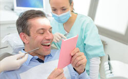 Man in dental chair looking at smile in mirror