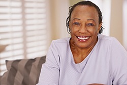 Smiling woman with dentures in Texarkana sitting on couch 