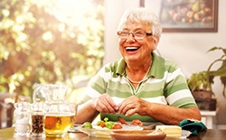 Senior woman at dining table smiling with dentures in Texarkana