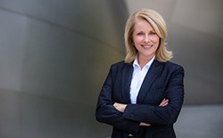 A middle-aged woman wearing a professional suit and standing with her arms crossed, smiling about her new dental implants