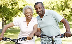 An older couple outside riding their bikes and smiling to show off their healthier teeth 