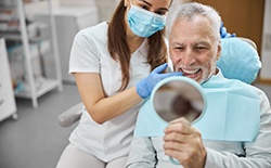 An older man admiring his new dental implants in a hand mirror