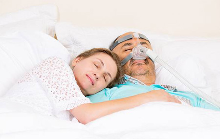 Woman sleeping in bed with man wearing a CPAP mask