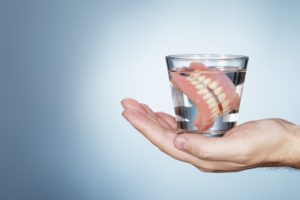 hand holding a glass of water with two full dentures soaking in it